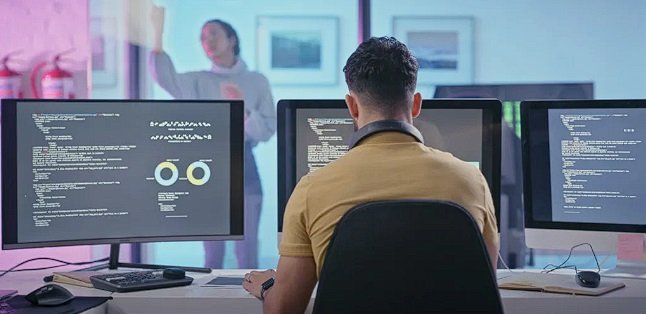 a man sitting at a desk with two monitors